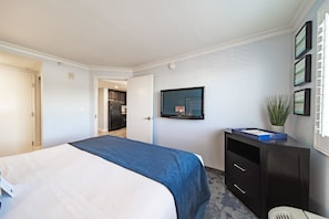 Ein Hotelzimmer mit einem Bett, einem an der Wand montierten Fernseher, einem Schreibtisch mit Schubladen und einer Zimmerpflanze.