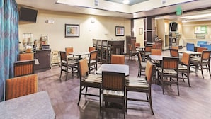 A hotel dining area with multiple tables and chairs, a television, and framed artwork on the walls. - Houston Hobby Airport (Houston)