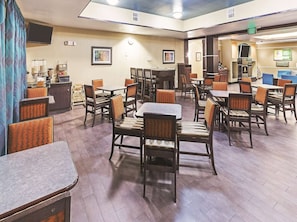 A hotel dining area with multiple tables and chairs, a television, and framed artwork on the walls.