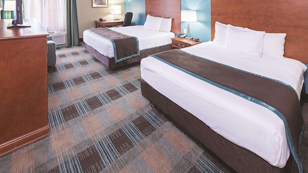 A hotel room with two beds, a desk, a chair, a lamp, and a window with curtains. - Houston Hobby Airport (Houston)