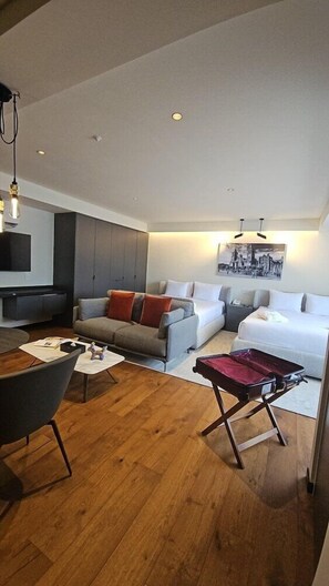 A modern hotel room with a wooden floor, a sofa, a bed, a small table, and a wall-mounted TV. - Amberes 64, an Ascend Collection Hotel (Mexico City)