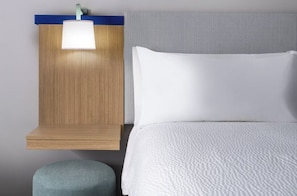 A hotel room with a bed, a nightstand with a lamp, and a small stool. - Garner Hotel Glen Burnie BWI Airport Area (Glen Burnie)