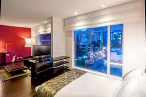 A hotel room with a bed, a TV, a desk, and a large window with a city view. - Hotel Sercotel Richmond Suites (Bogotá)