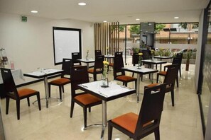 A restaurant with tables and chairs, a projection screen, and a view of the outside. - Hotel Sercotel Richmond Suites (Bogotá)