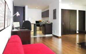 A modern living room with a red sofa, a small kitchen area with dark cabinets, and a dining area with a black chair. - Hotel Sercotel Richmond Suites (Bogotá)