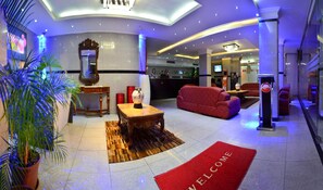 A hotel lobby with a reception desk, a red sofa, a wooden coffee table, and a welcome mat. - Grand International Hotel (Panama City)
