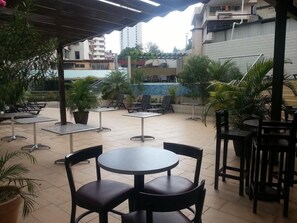 An outdoor patio area with round tables and chairs, a pool, and surrounding greenery. - Grand International Hotel (Panama City)