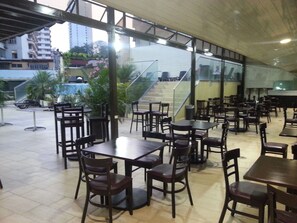 Un espace de restauration intérieur avec des tables et des chaises, un escalier et une vue sur les bâtiments environnants.