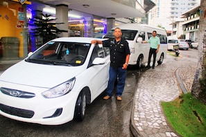 Un coche blanco estacionado en una calle mojada, con un edificio al fondo.
