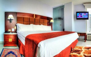 Een hotelkamer met een groot bed, een televisie, een kledingkast en een bureau met een lamp.