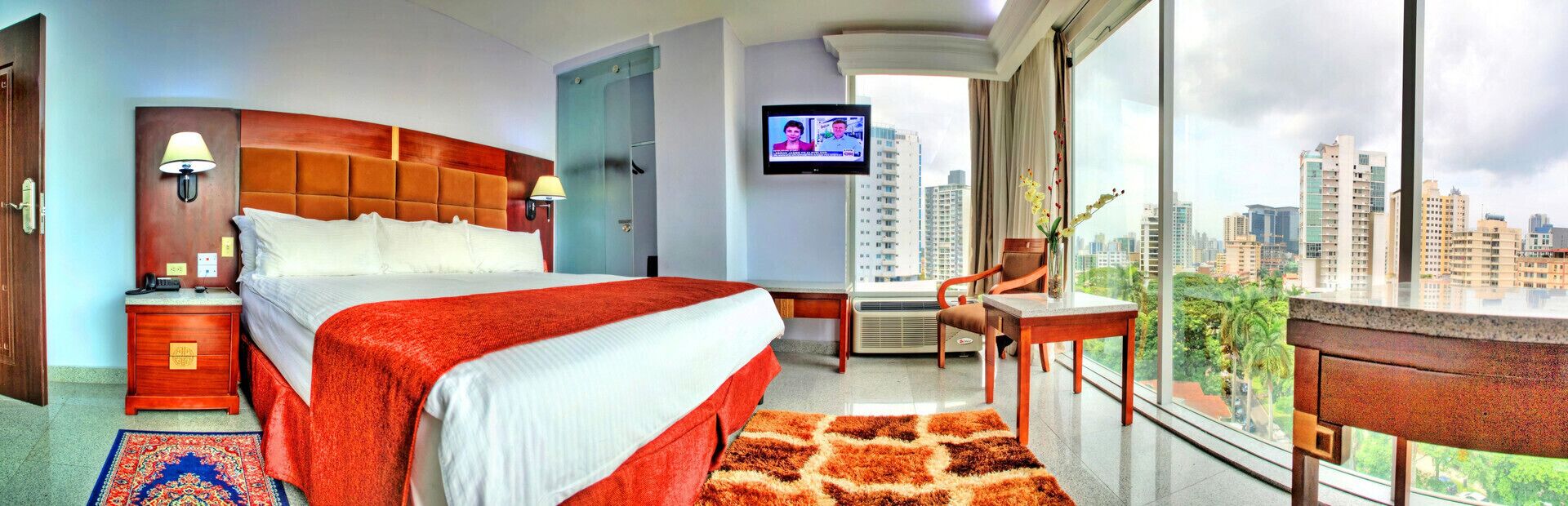 Camera d'albergo con un letto grande, televisione, una scrivania con sedia e vista sulla città.