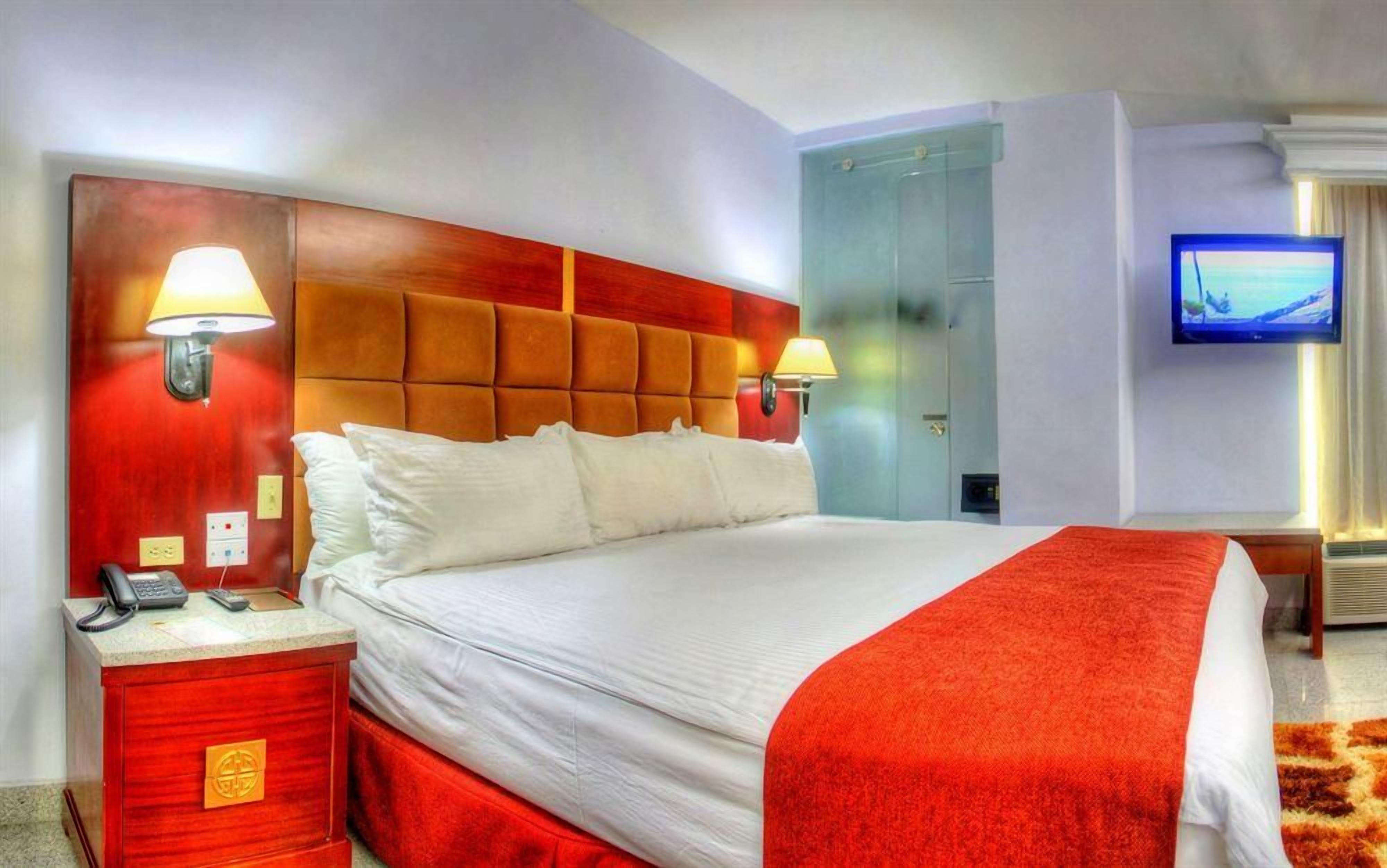 Una camera d'albergo con un letto grande, due lampade da comodino, una televisione e un armadio.