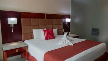 A hotel room with a large bed, two bedside tables, a headboard, and wall-mounted lights.