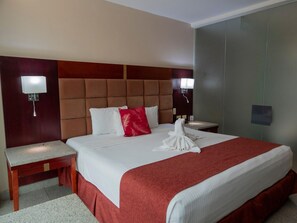 Habitación de hotel con una cama grande, dos mesitas de noche, cabecera y luces fijadas a la pared.