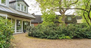 Ein modernes Haus mit einer überdachten Veranda, einem großen Baum und dichtem Buschwerk.