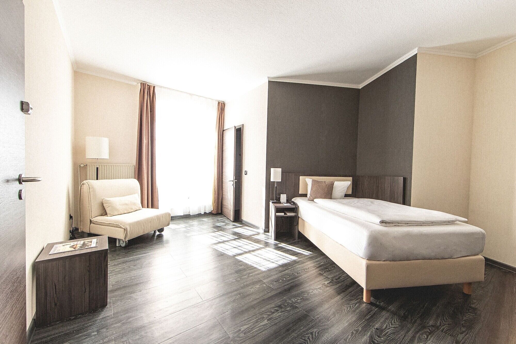 A hotel room with a bed, a chair, a nightstand, and a desk.