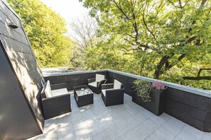 Eine Dachterrasse mit Gartenmöbeln und Blick auf Bäume.
