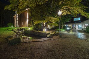 A nighttime view of a building with a pond, surrounded by trees and a gravel path. - Hotel Schmoeker-hof (Norderstedt)