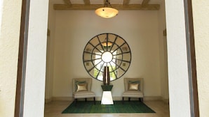 A hallway with a large circular mirror, two chairs, a floor lamp, and a ceiling light.