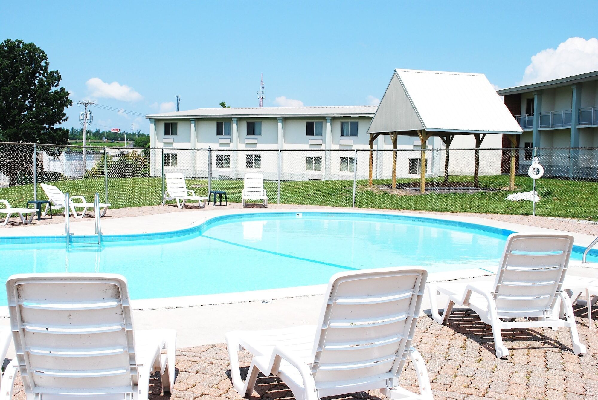 A swimming pool with lounge chairs, a fenced area, and a building with multiple windows in the background.