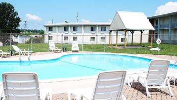 A swimming pool with lounge chairs, a fenced area, and a building with multiple windows in the background.