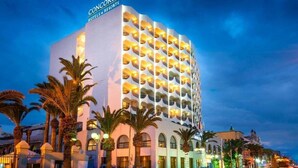 Un hotel de diseño moderno, con varios balcones y palmeras en primer plano.