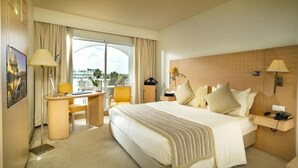 Habitación de hotel con una cama grande, un escritorio, una silla, una lámpara y vistas a la ciudad.