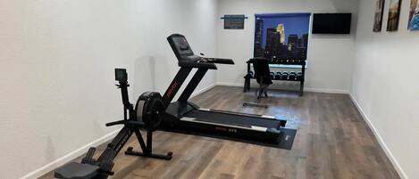 A home gym with a treadmill, stationary bike, and rowing machine.