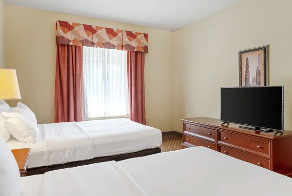 Habitación de hotel con dos camas, un televisor sobre un aparador de madera y una ventana con cortinas.