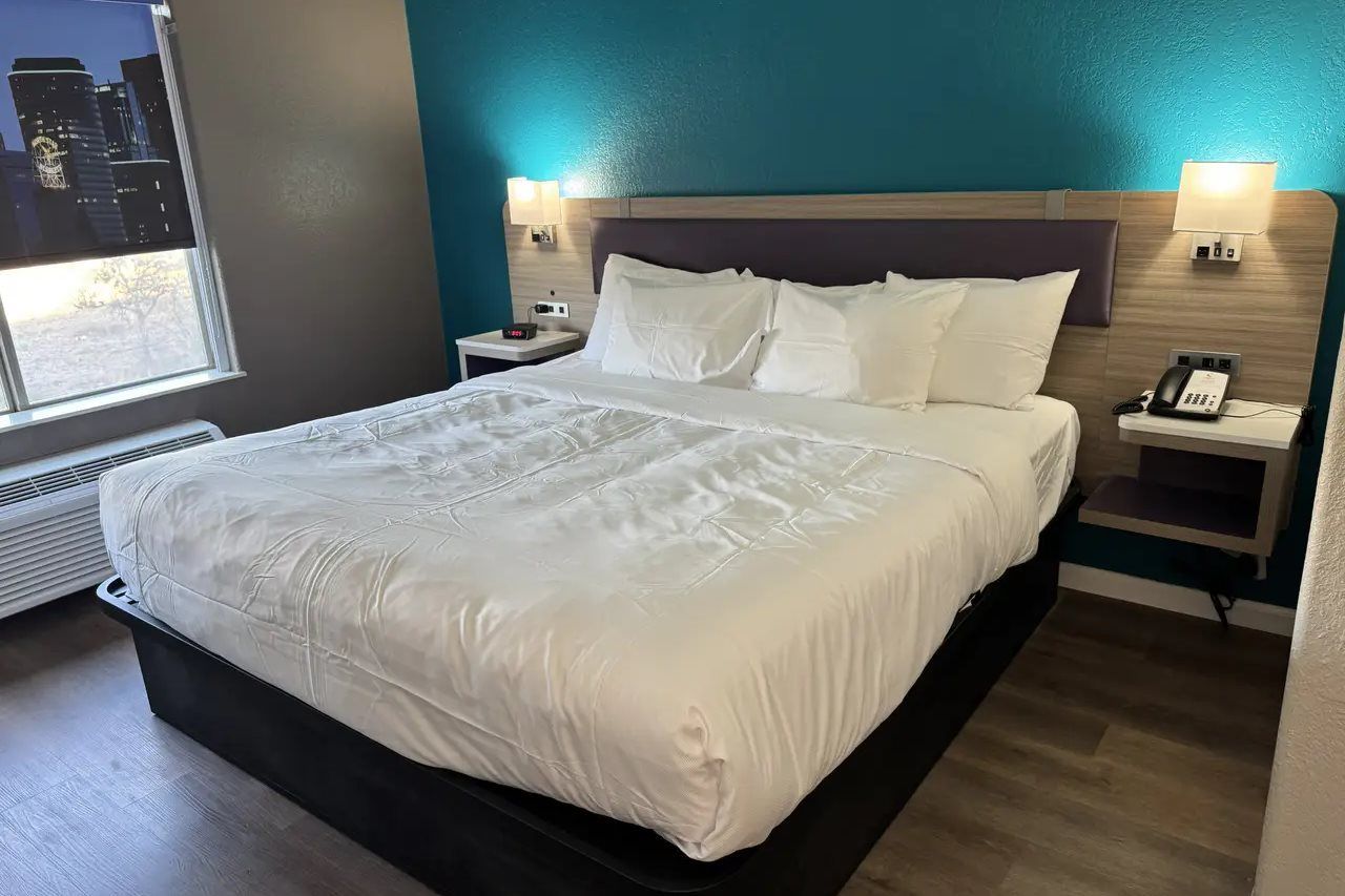 A hotel room with a large bed, a nightstand, a phone, and a window with a city view.
