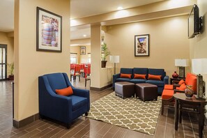 A hotel lobby with a blue armchair, a sofa set, a patterned rug, and a dining area in the background. - Red Roof Plus+ San Antonio Northeast (San Antonio)