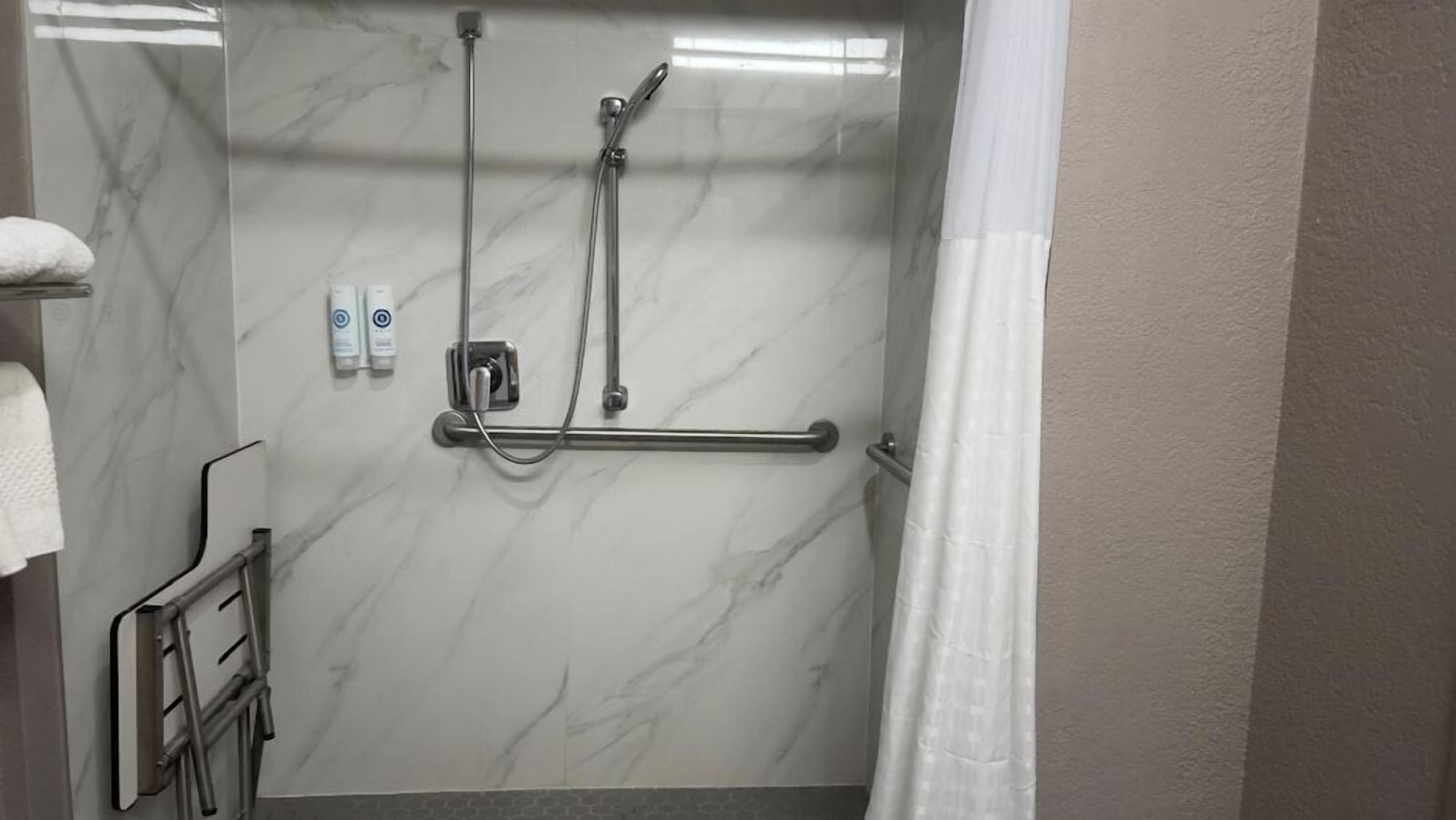 A bathroom with a shower, grab bars, and a towel rack.