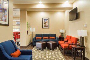 A hotel room with a blue sofa, orange cushions, a patterned rug, a flat-screen TV, and a dining area with red chairs. - Red Roof Plus+ San Antonio Northeast (San Antonio)