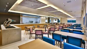 Un área de comedor moderna con varias mesas y sillas, una barra con una máquina de café, y un ventanal que ofrece vistas.