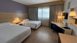 Habitación de hotel con dos camas, un escritorio, una silla, un televisor y una ventana con cortinas.