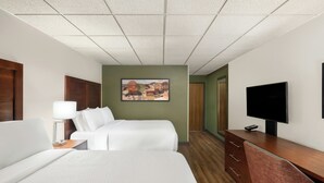 Quarto de hotel com duas camas, uma escrivaninha, televisão e um quadro na parede.