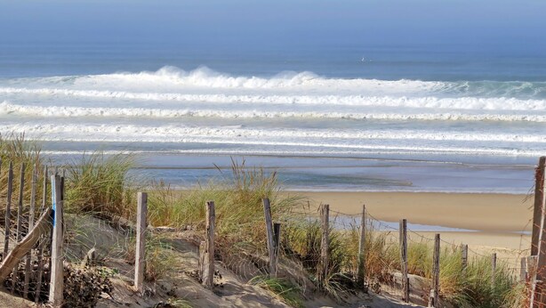 Una playa con olas, una orilla de arena y una valla de madera.