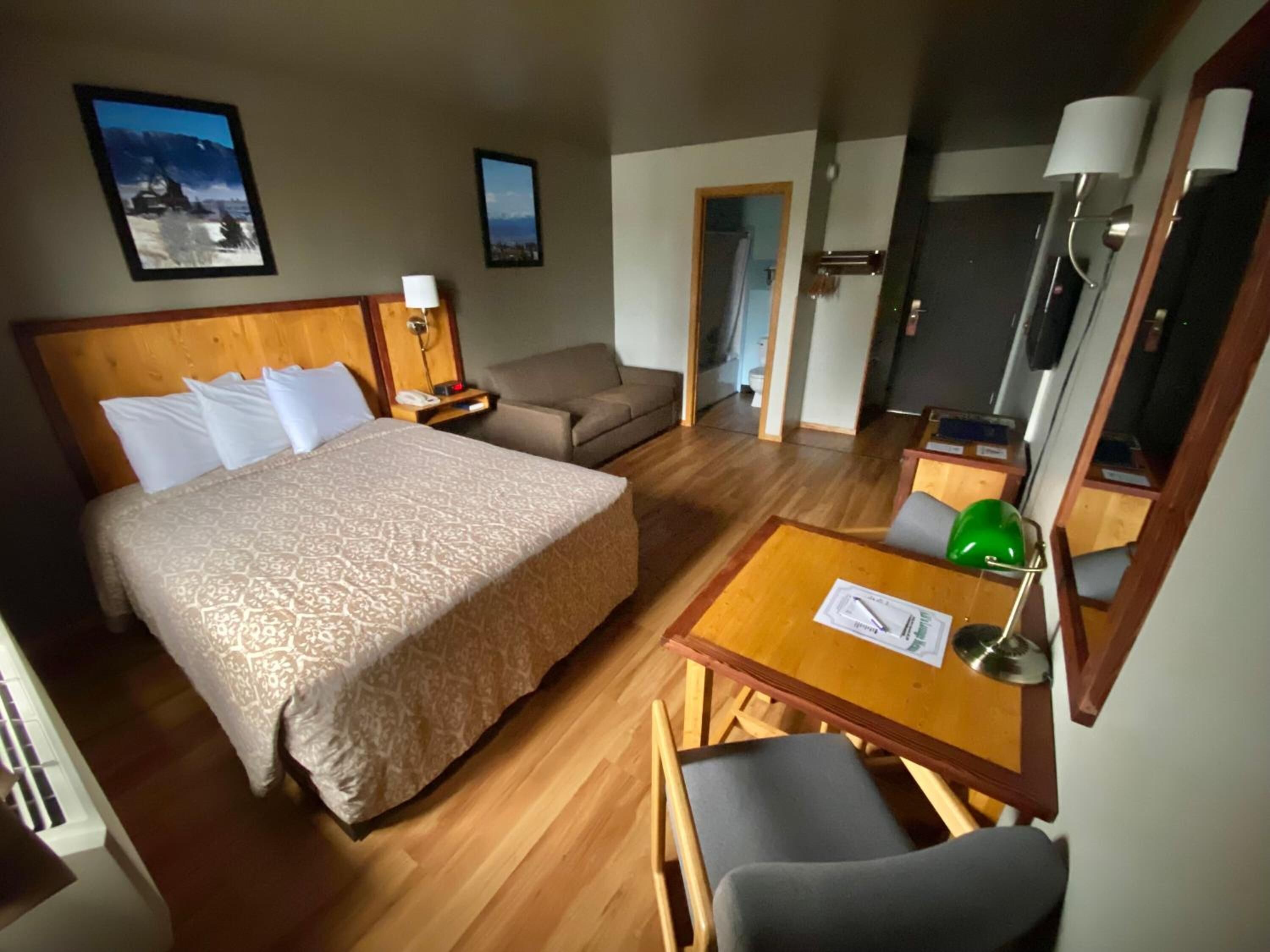 Habitación de hotel con cama, sofá, escritorio con lámpara y dos cuadros en la pared.