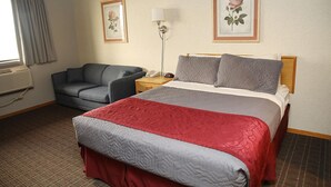 Une chambre d’hôtel avec un lit, un canapé, une table de chevet avec une lampe, et deux tableaux représentant des motifs floraux, encadrés et accrochés au mur.