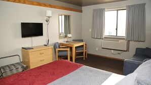 Une chambre d’hôtel comprenant un lit, un bureau avec une chaise, une télévision, un miroir, un climatiseur et une fenêtre avec des rideaux.