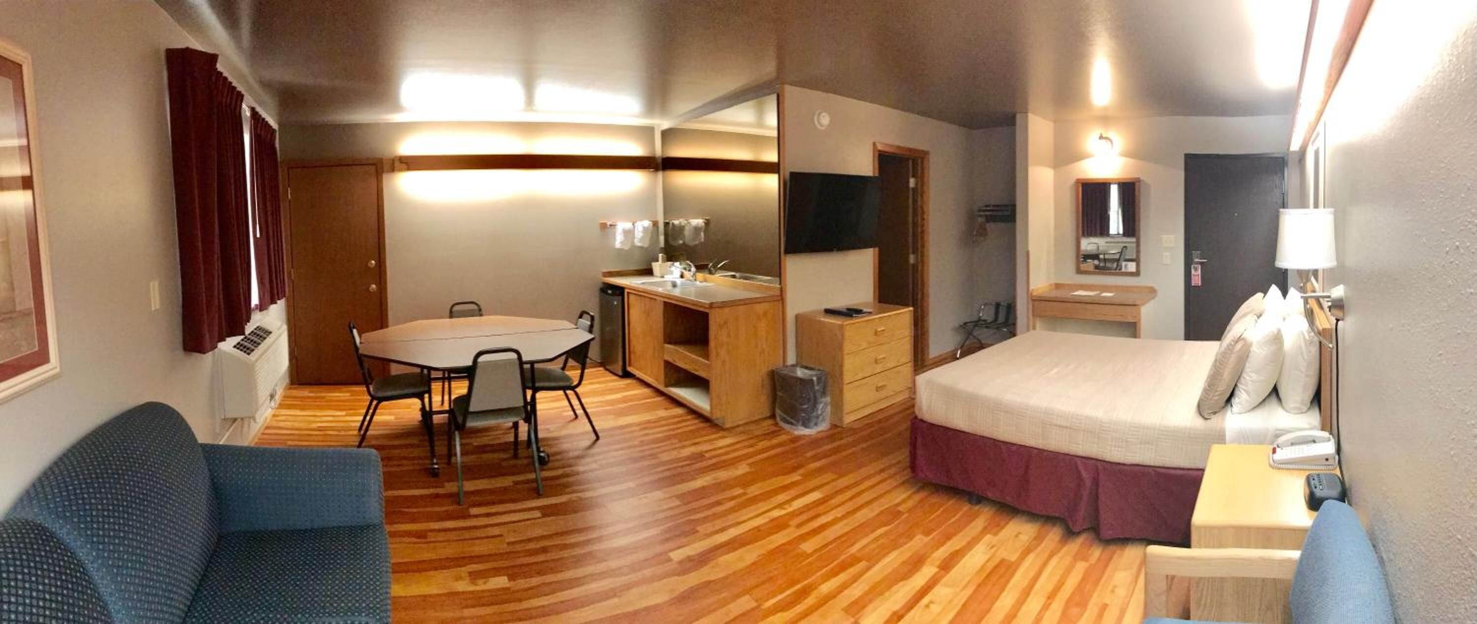 Habitación de hotel compacta con cama, escritorio con silla, una mesita, espejo y sofá.