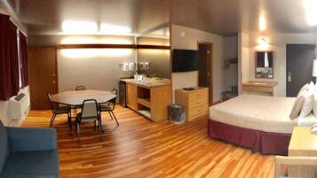 Habitación de hotel compacta con cama, escritorio con silla, una mesita, espejo y sofá.