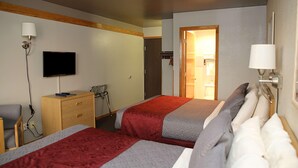 Une chambre d’hôtel avec deux lits, une télévision, un bureau avec des tiroirs et une chaise.