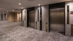 Un vestíbulo de hotel con piso alfombrado, ascensores y un diseño moderno.