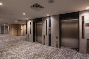 A hotel lobby with a carpeted floor, elevators, and a modern design. - Mtree Hotel (Puchong)