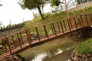 A wooden bridge over a pond with a stone border, surrounded by greenery and a fence. - Samba Foz do Iguassu (Foz do Iguaçu)