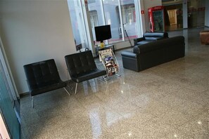 Een wachtruimte met zwarte stoelen, een tijdschriftenrek en een Coca-Cola automaat.