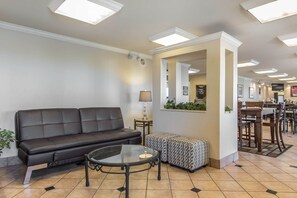 A lobby with a leather sofa, a glass-top table, patterned ottoman, and a mirror. - Econo Lodge Inn and Suites Joplin MO (Joplin)