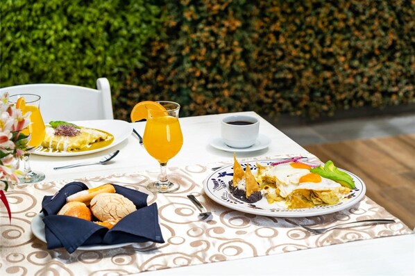 A breakfast setting with a plate of eggs, toast, and a glass of orange juice on a table with a patterned tablecloth. - Comfort Inn Puebla Centro Historico (Puebla)