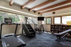 Academia com esteiras, aparelhos de escada e bicicletas ergométricas, equipada com tela digital e televisão.
